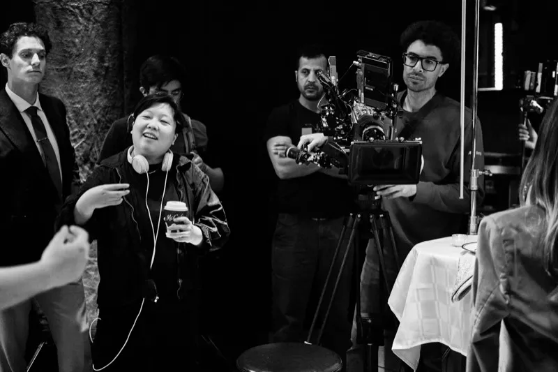Black and white photograph of a director in headphones with a coffee cup talking to crew beside a cinema camera.