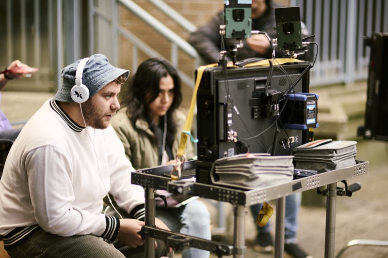 Boom operator holding a microphone above a scene in progress.