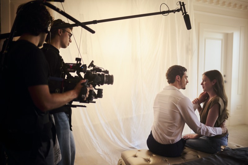 Boom operator holding a microphone above a scene in progress.