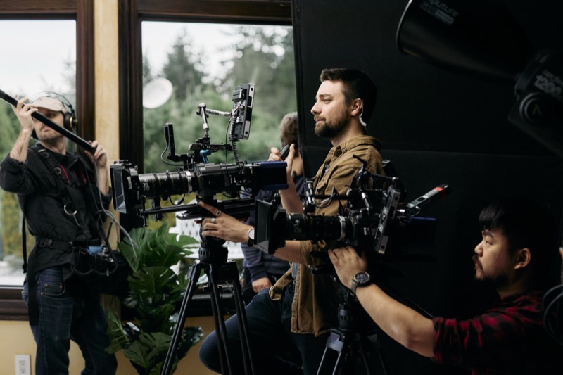Boom operator holding a microphone above a scene in progress.