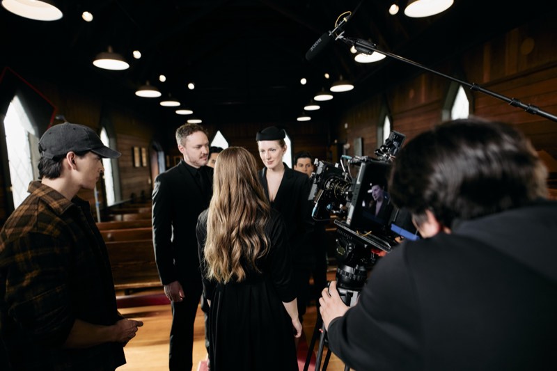 Boom operator holding a microphone above a scene in progress.