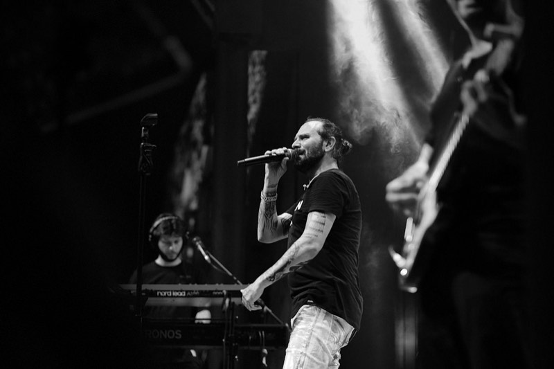 Black and white photograph of a vocalist mid-song on a darkened stage.