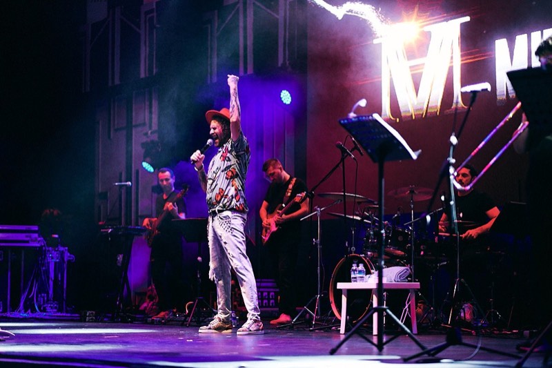 Singer at the microphone under coloured stage lighting.