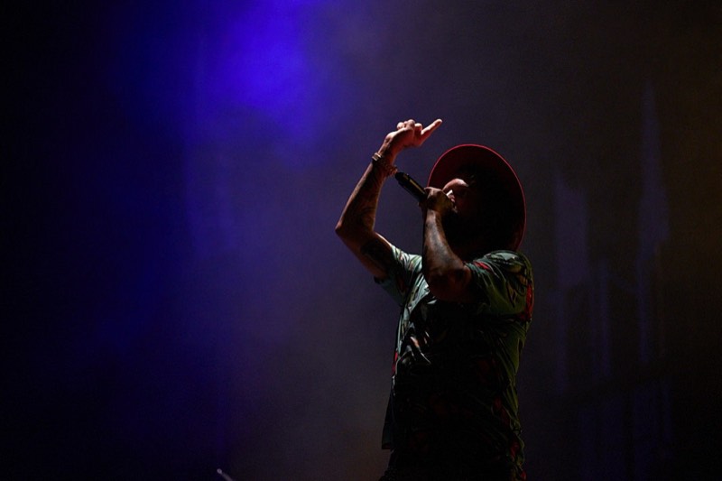 Black and white photograph of a vocalist mid-song on a darkened stage.