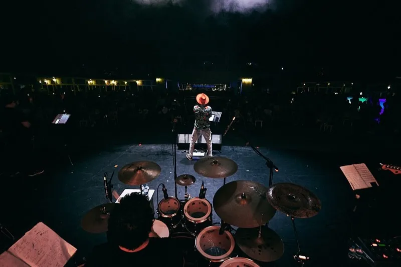 The stage from behind the drum kit at night, the singer alone at the front and the audience beyond.