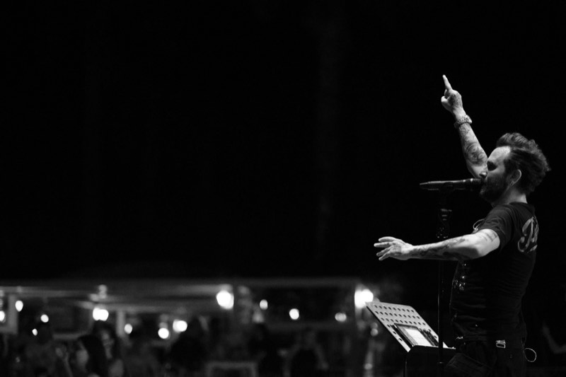 Black and white photograph of a vocalist mid-song on a darkened stage.
