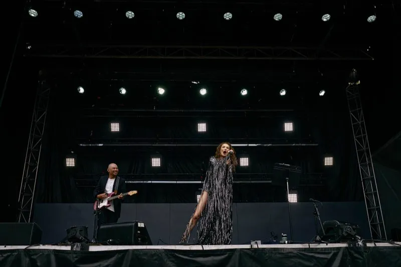 A wide shot of a two-piece act on a festival stage under a rig of white lights.