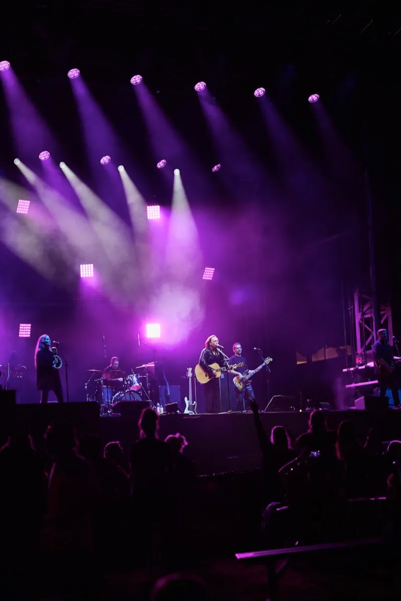 A band on stage under purple beams, the guitarist at the microphone and the crowd in silhouette.