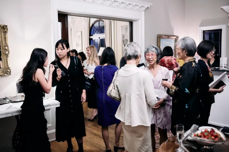 Guests talk in small groups by a doorway, drinks in hand.