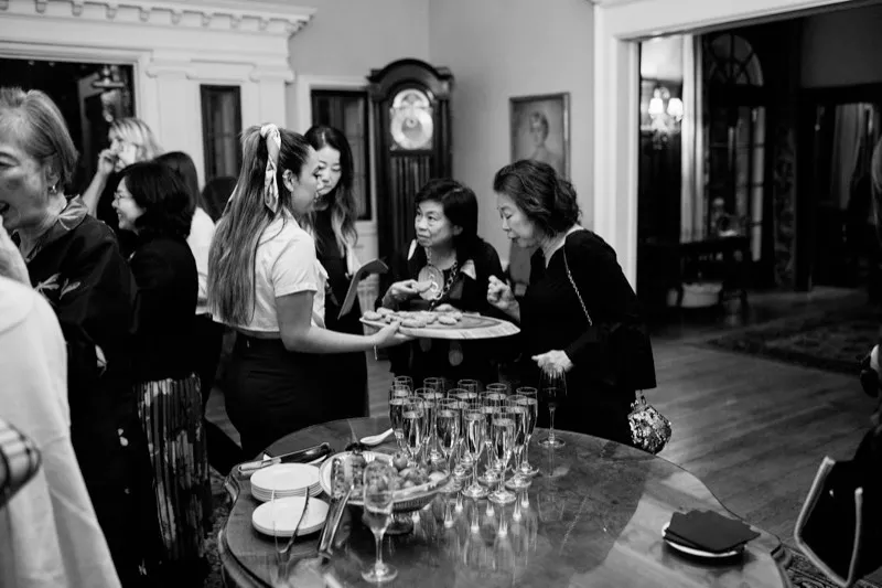 Black and white photograph of guests around a table of champagne flutes and canapés.