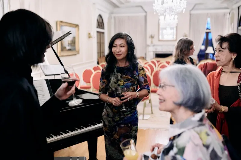 Guests chat beside a grand piano, the front row of chairs behind them.