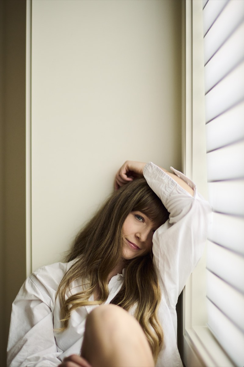 Natural-light portrait against a plain wall, relaxed posture.