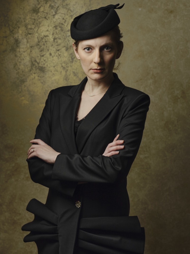 Natural-light portrait against a plain wall, relaxed posture.