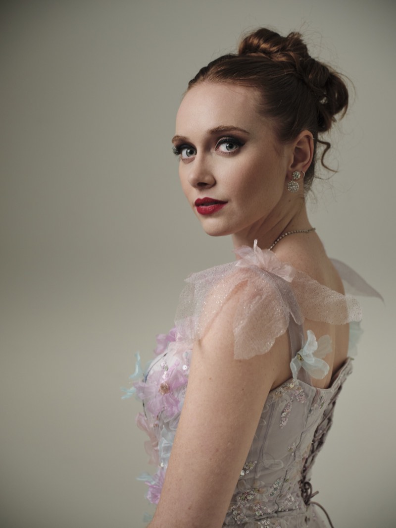 Natural-light portrait against a plain wall, relaxed posture.
