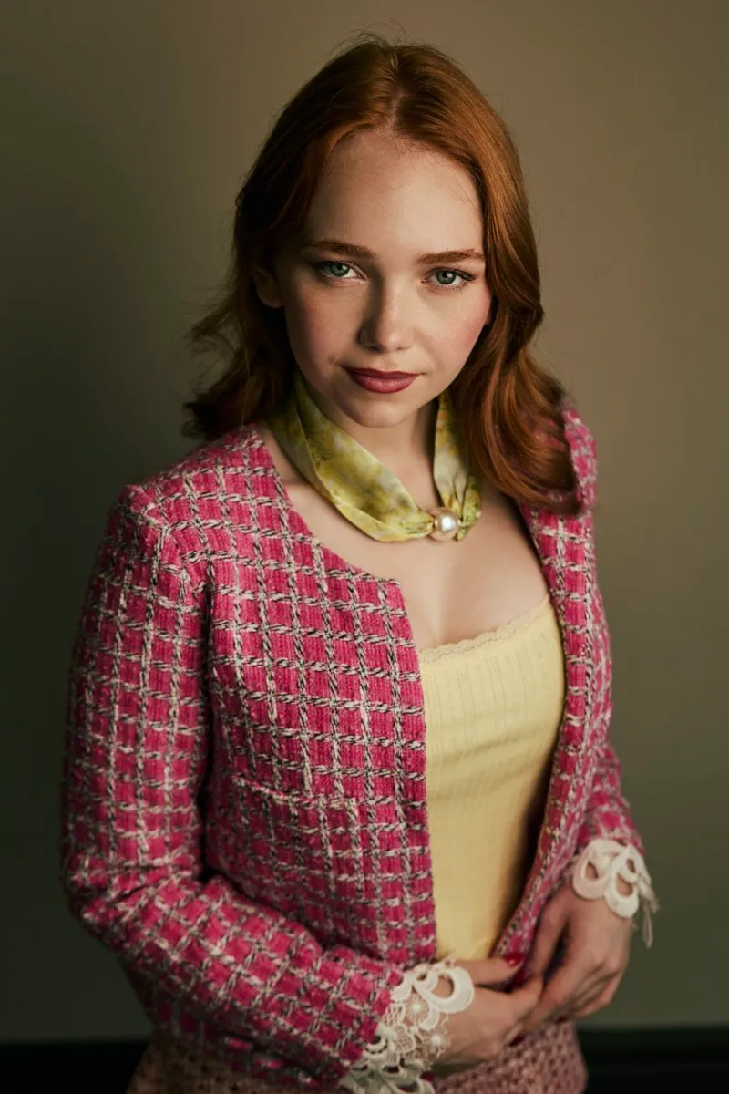 Headshot of a red-haired woman in a pink tweed jacket and yellow top with a silk scarf, smiling at the camera.