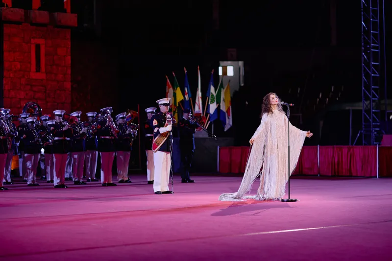 MAKENZA opens her arms wide in front of the band and the row of flags.