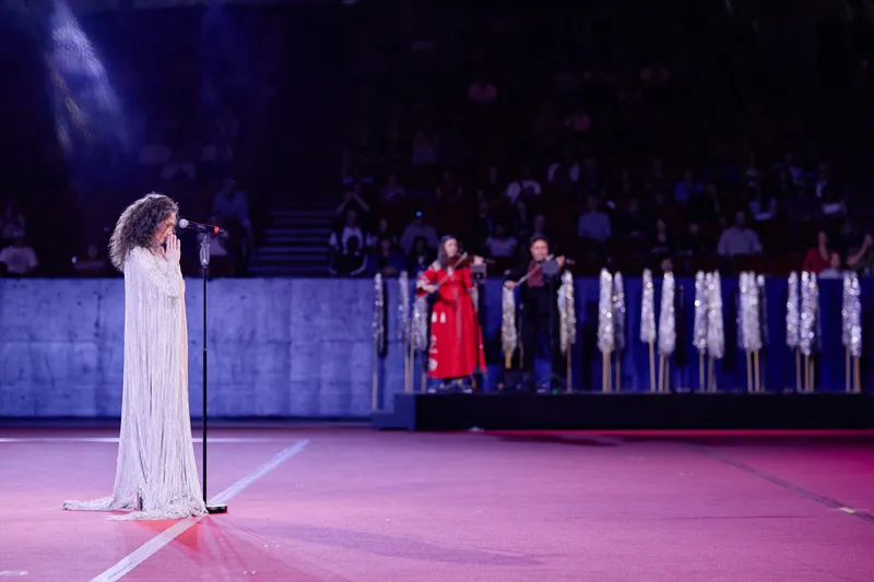 MAKENZA at the microphone, the violinists and the singers in white on the riser behind.