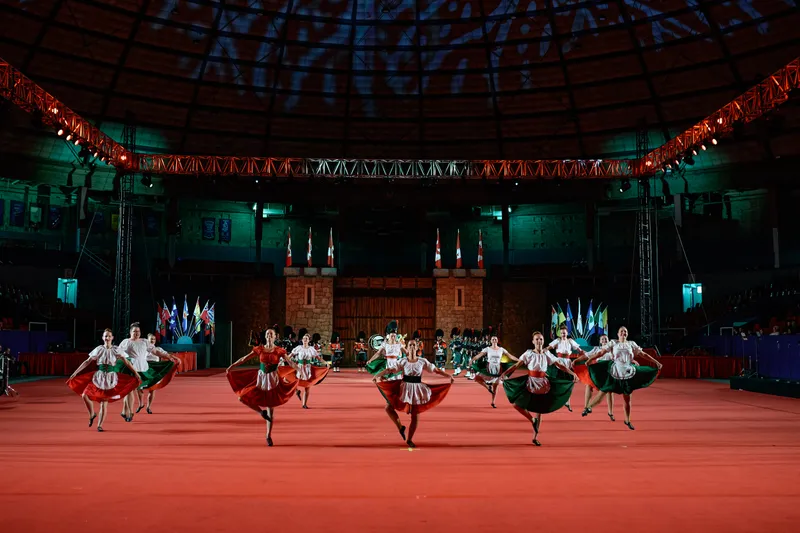 Dancers in green and red skirts spin on the red floor in front of the castle set.