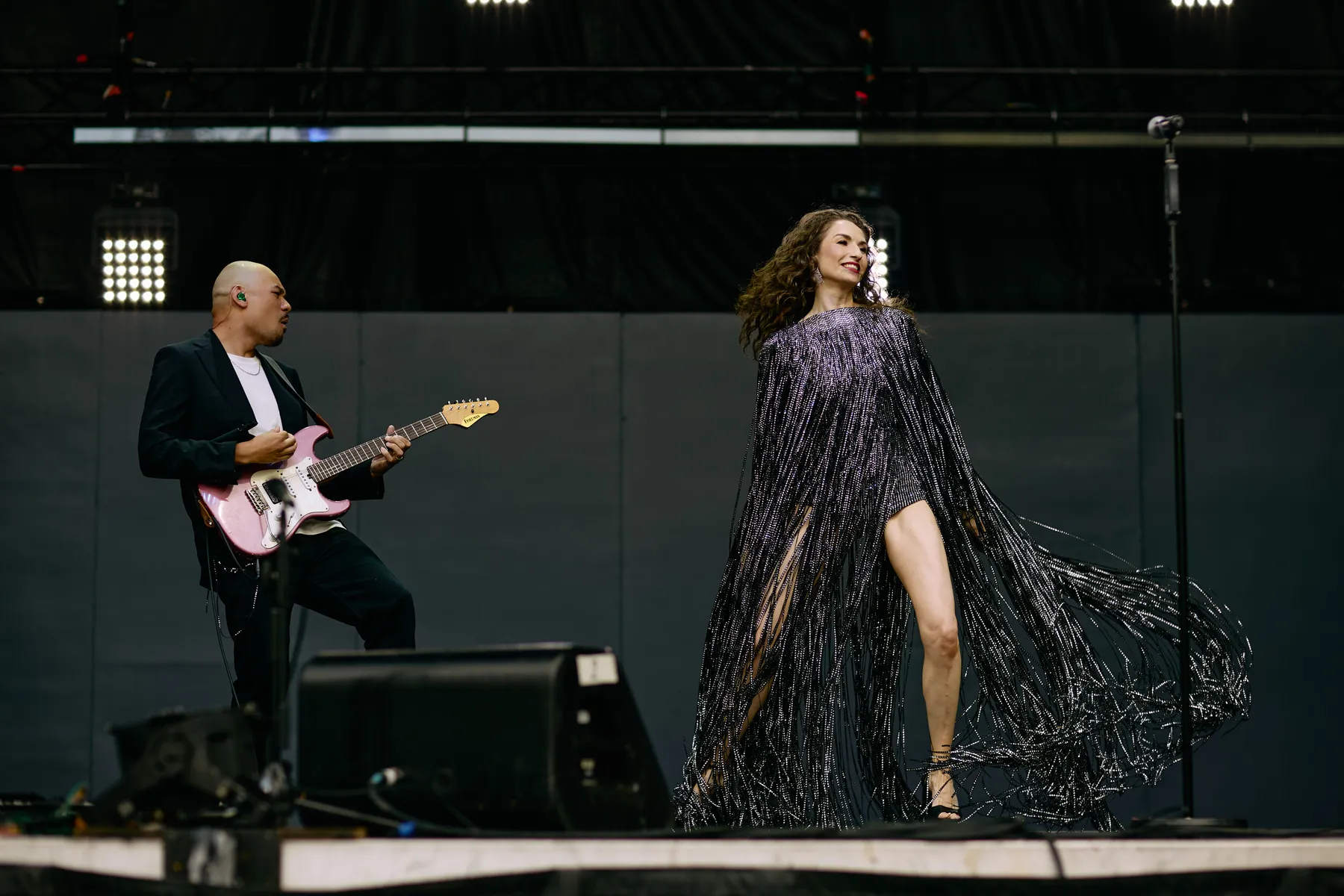 MAKENZA on the BCAA Stage at the PNE Fair, the fringed dress flaring as she steps across the stage, the guitarist with the pink guitar at her left.