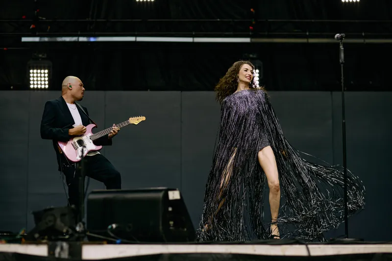 The dress flares out as MAKENZA steps across the wide stage, the guitarist watching.