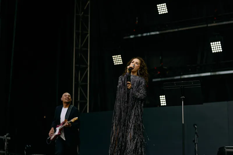MAKENZA sings the first song at the microphone in a long fringed dress, the guitarist at her left.