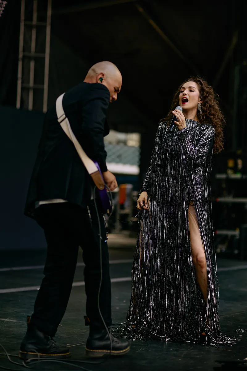 MAKENZA sings into the microphone while the guitarist bends low over his guitar.