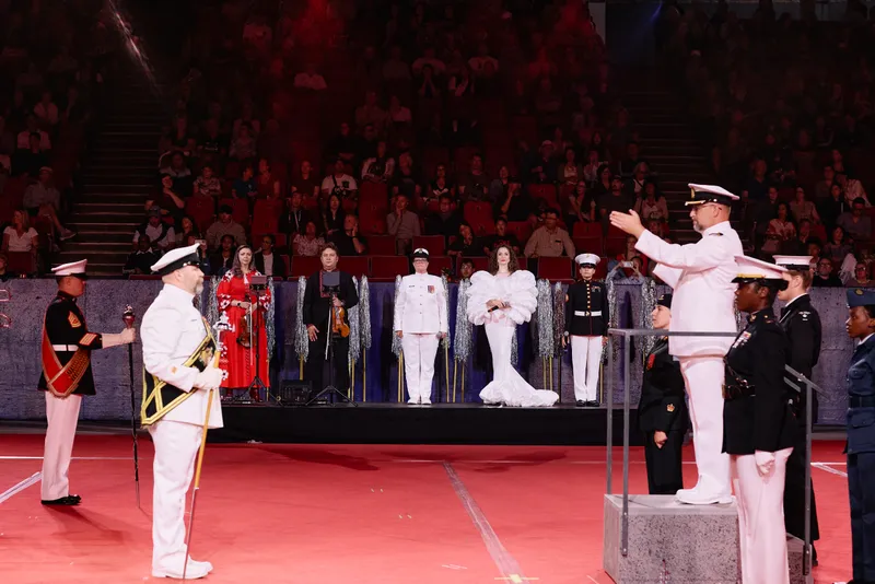 MAKENZA on the riser in a white ruffled dress as the officers salute at the front.