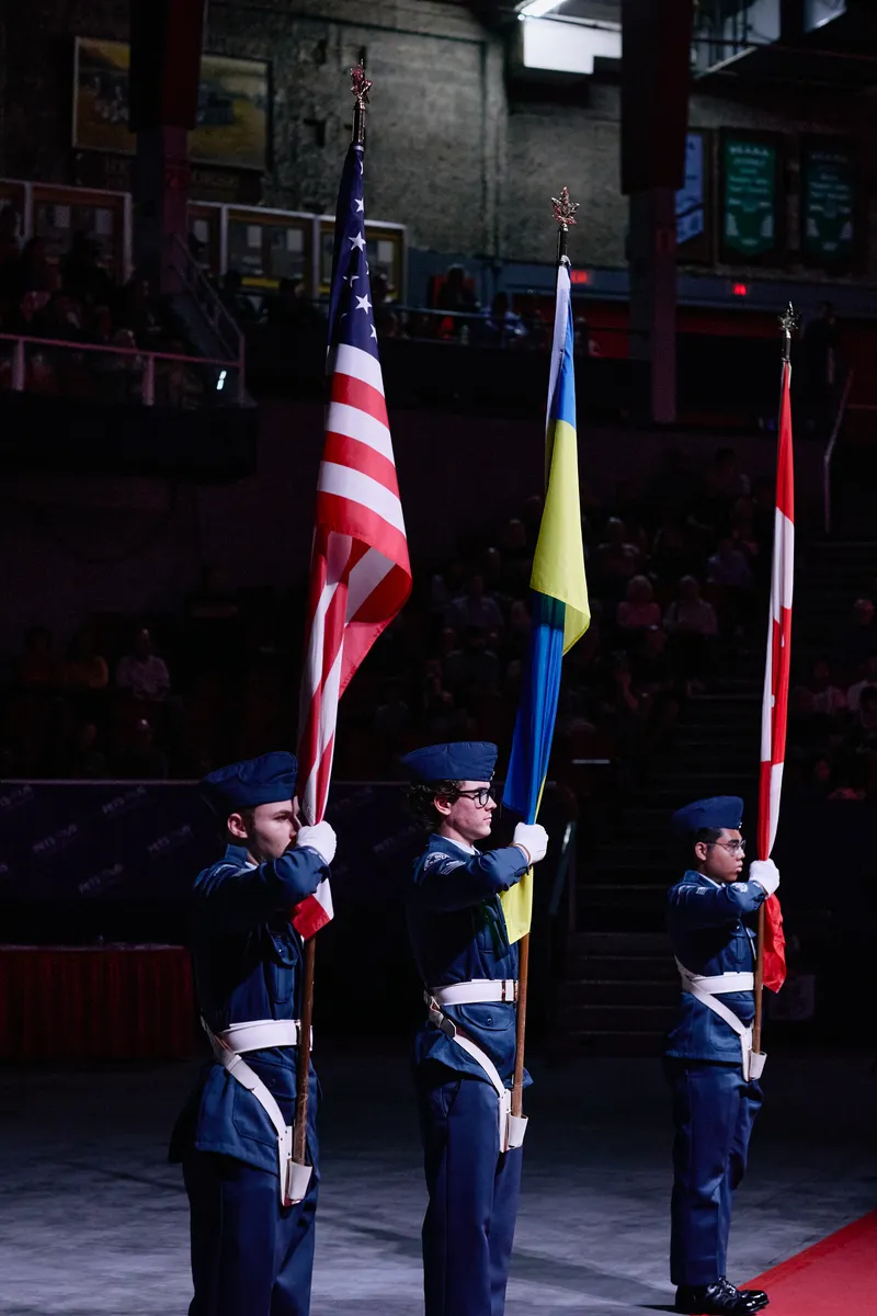 Three flag bearers stand to attention with their flags on the red floor.