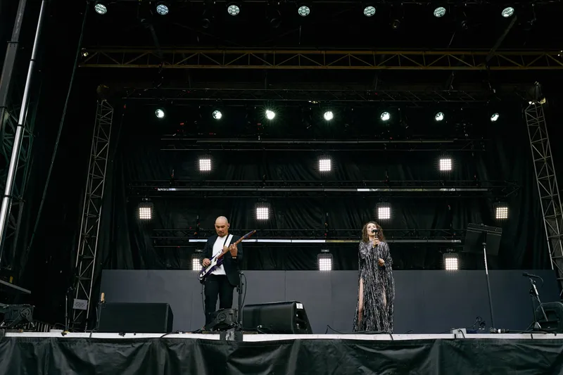 The singer and the guitarist stand small on the wide stage beneath the lighting rig.