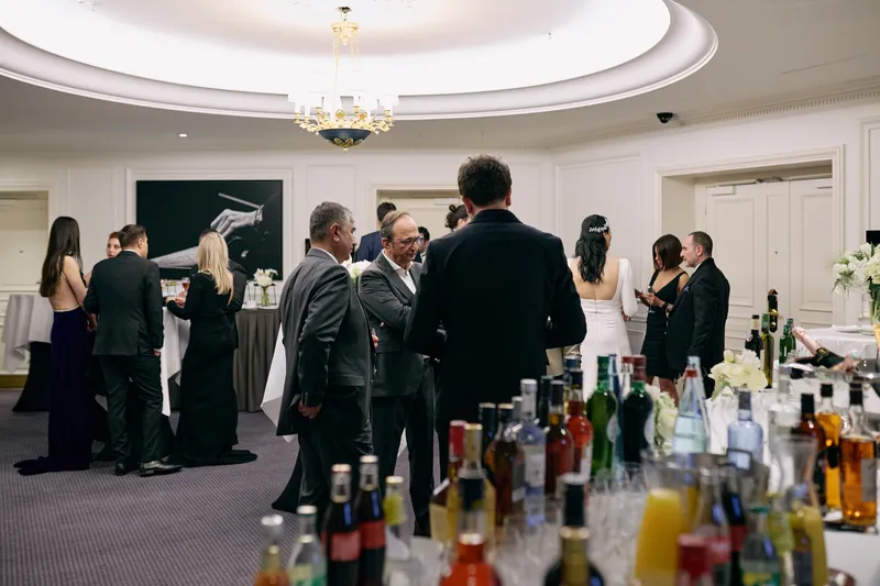 Rows of bottles on the bar with guests gathered behind them.