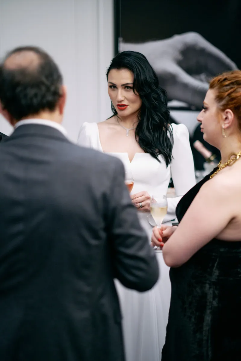 Julie, dark hair and red lipstick, in conversation with two guests, a glass in her hand.