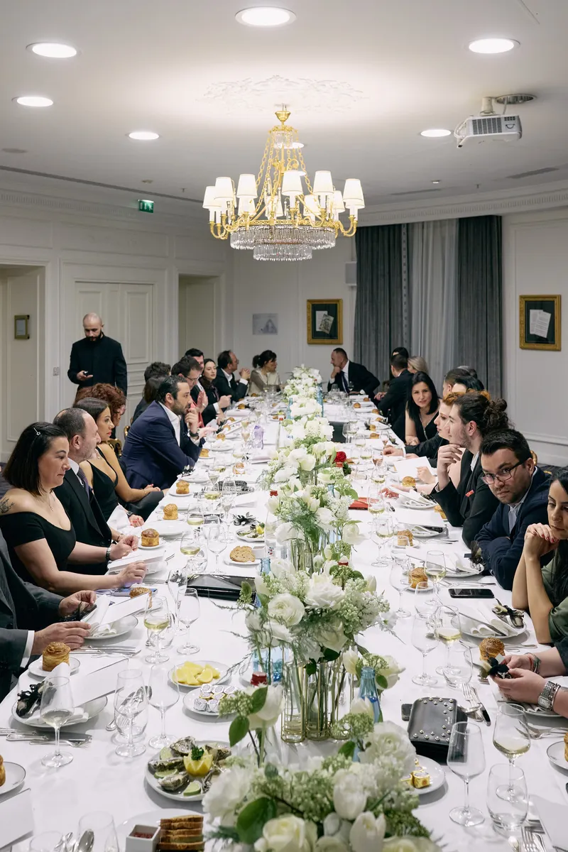 The dinner table seen from above and behind the guests, the flowers running down its centre.