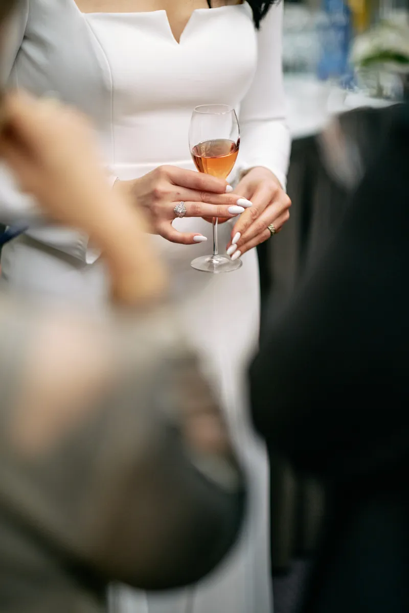 A guest's hand holding a glass of rose wine, the rest of the room soft behind it.