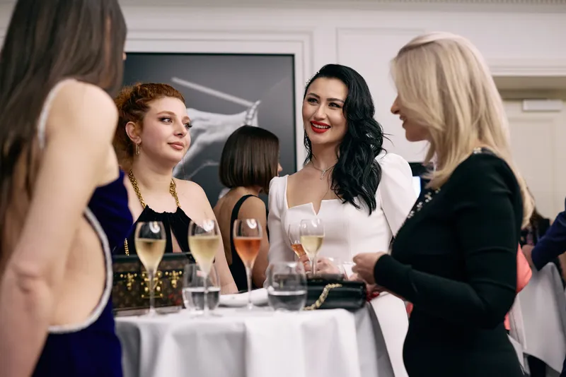 Two guests in long dresses talk by the bar beneath the framed photograph.
