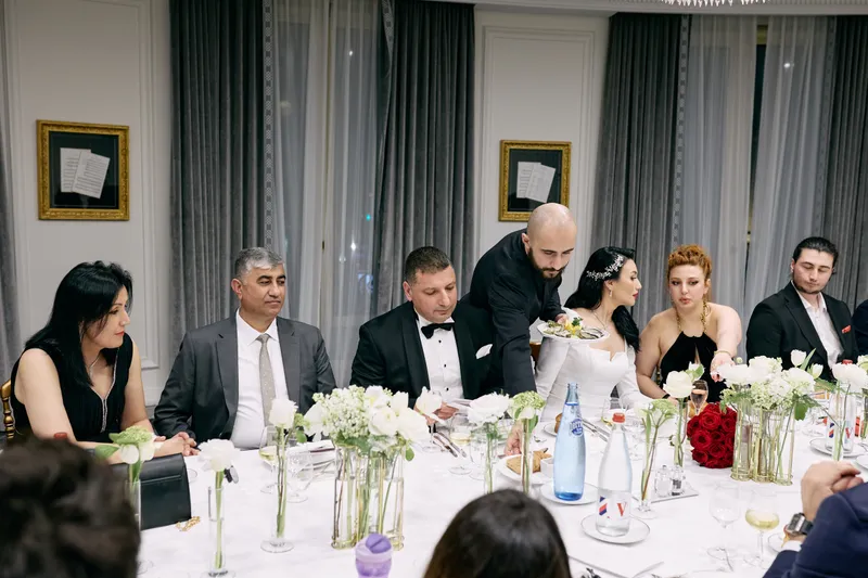 Guests settle along the dinner table, talking across the flowers.