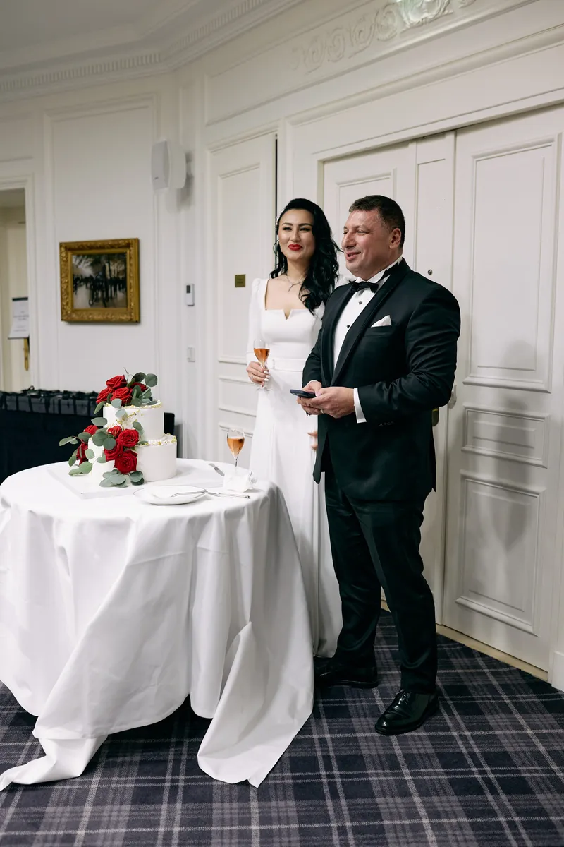 Michael and Julie stand together at the small cake table with its red roses.