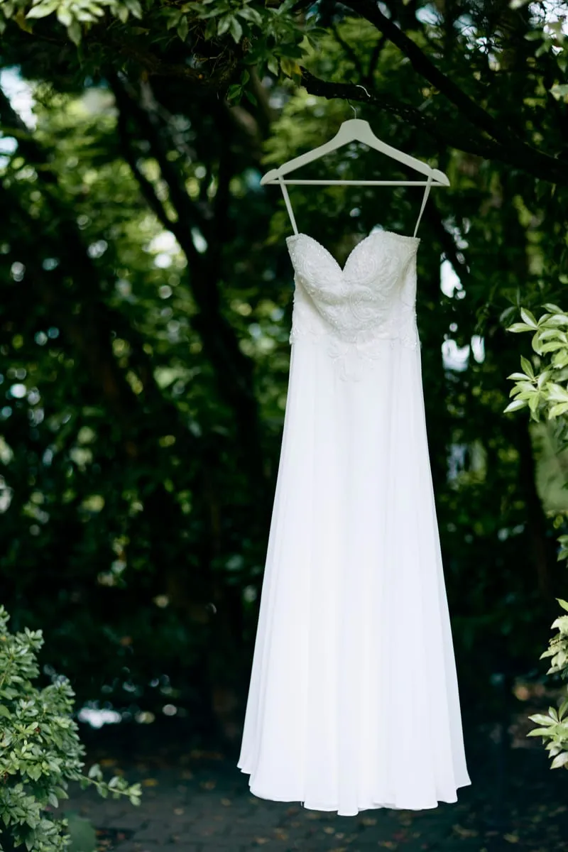 The wedding dress on a hanger in the garden, under the trees.