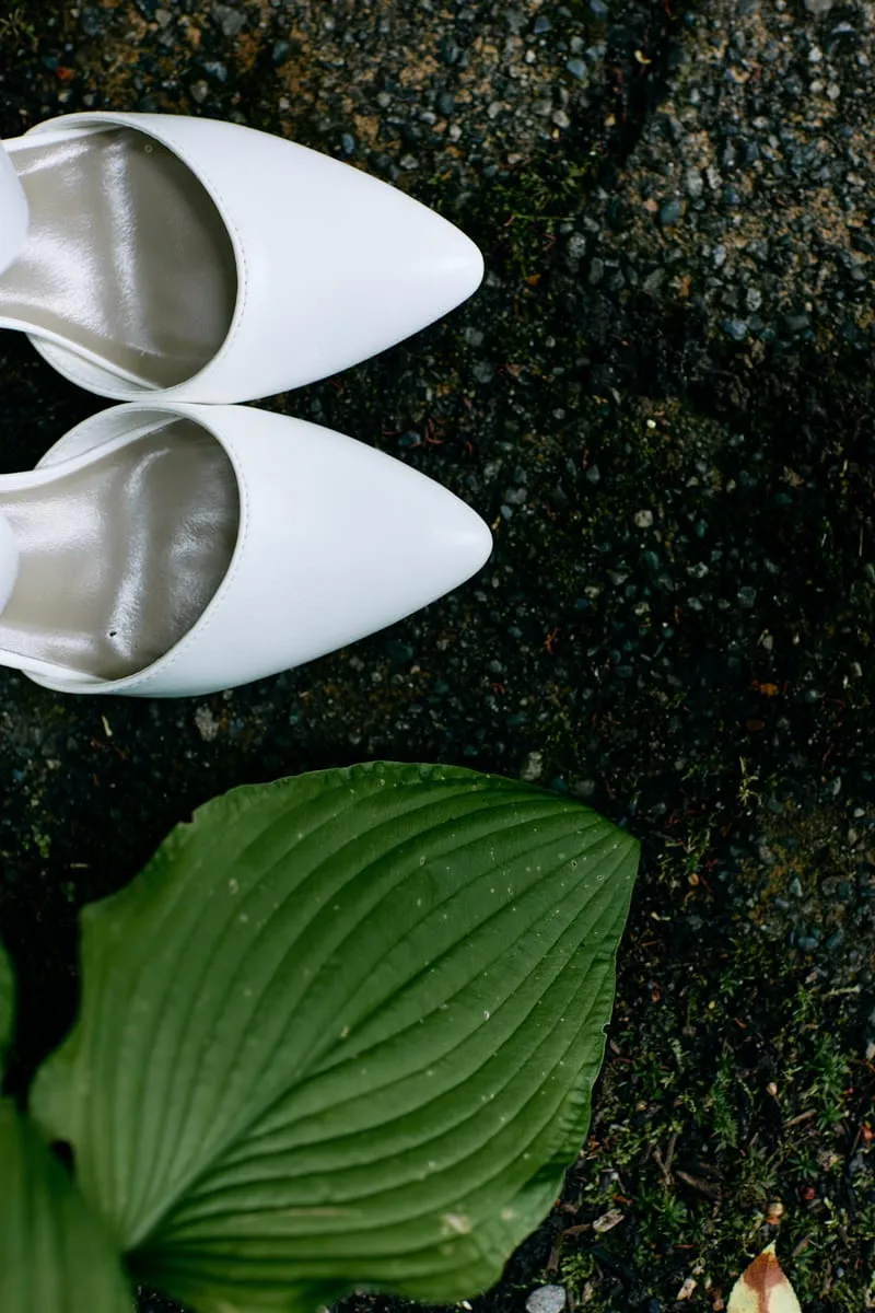 White pointed heels on wet dark stone beside a hosta leaf.