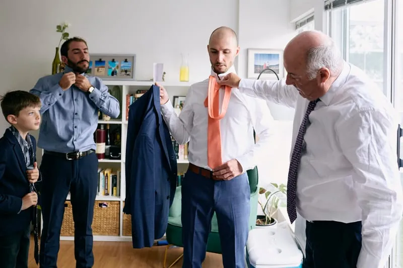 Two men helping James into his jacket in the kitchen.