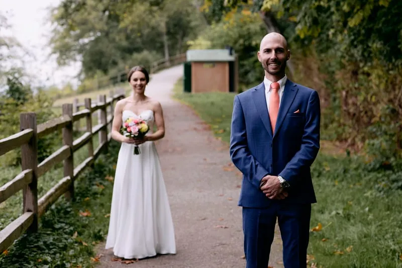 Olivia walking up a fenced forest path towards James, who waits with his back turned.
