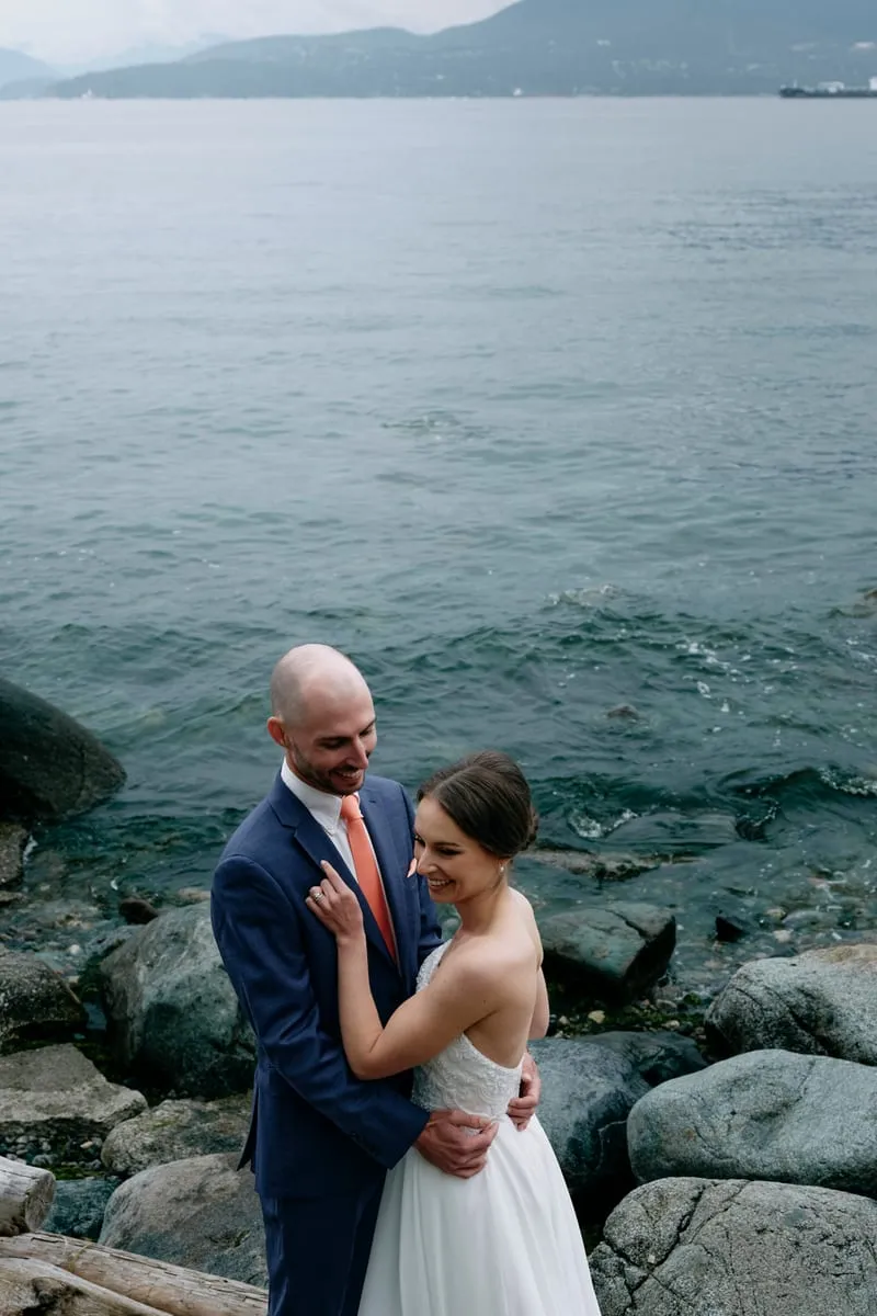 Olivia and James on the rocks at the water's edge, mountains across the bay.