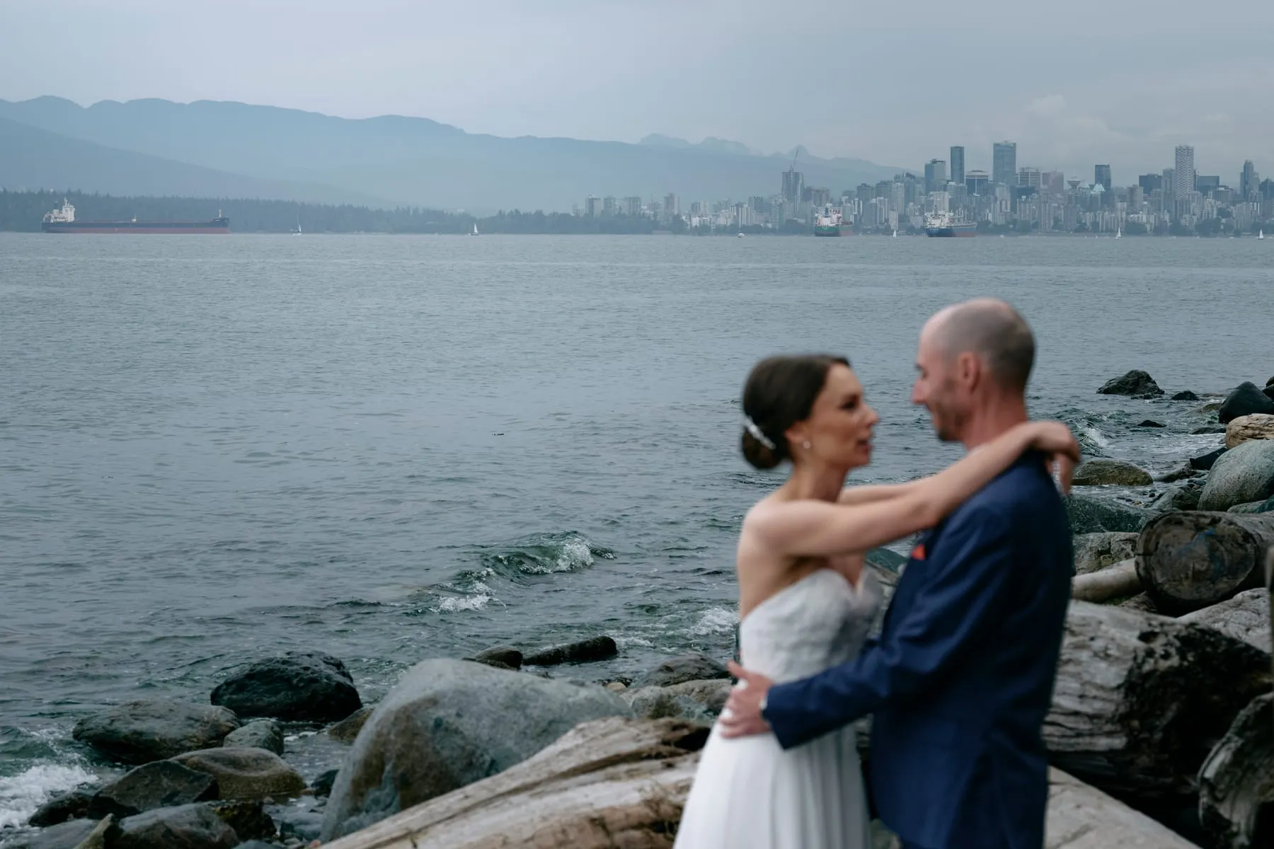 Olivia and James on the beach with the Vancouver skyline across the water.