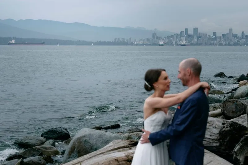 Olivia and James on the beach with the Vancouver skyline across the water.