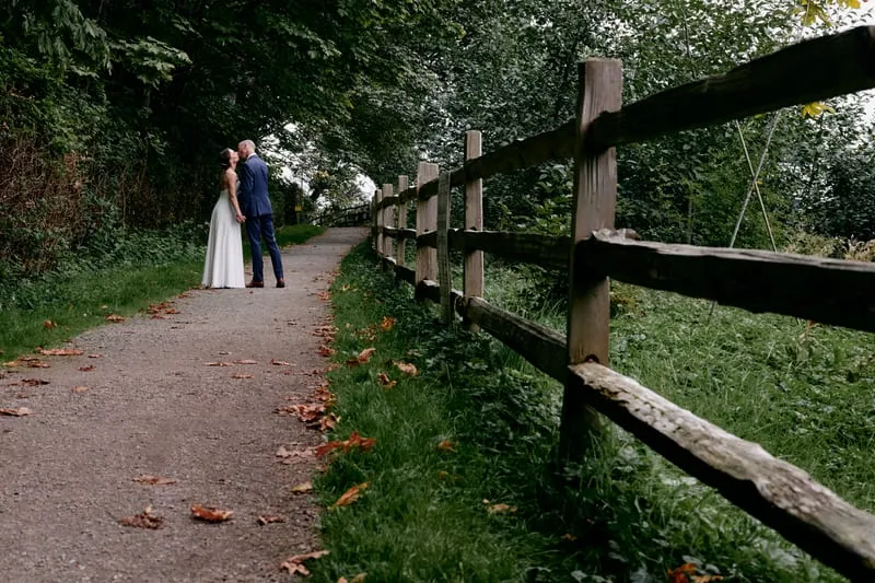 A long fenced path through the forest, the couple small in the distance.
