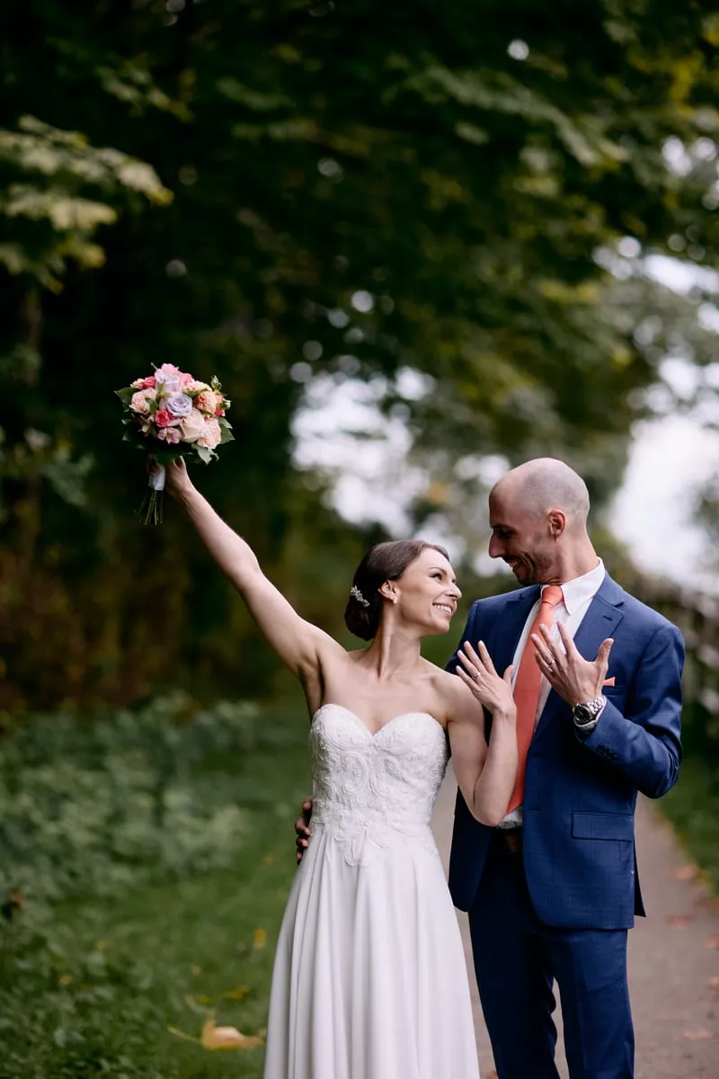 Olivia holding the bouquet up in the air on the path, James laughing.