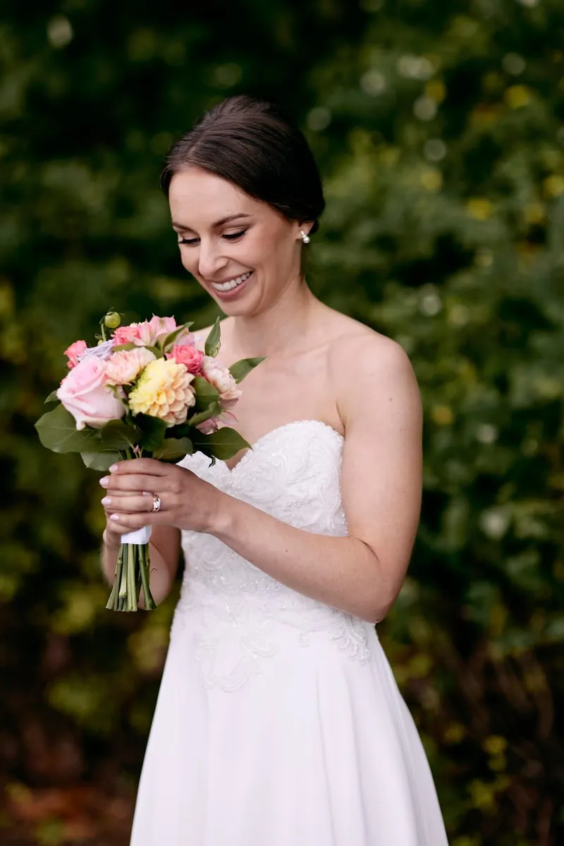 Olivia laughing down at her bouquet of pink, yellow and lilac flowers.