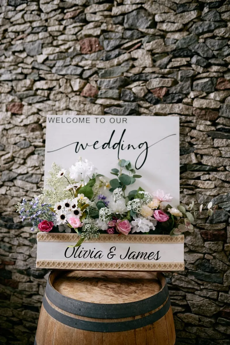 A welcome sign reading Olivia and James beside a bouquet on a barrel.