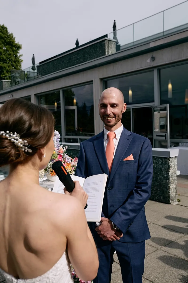 Olivia reading her vows into a microphone, James smiling.
