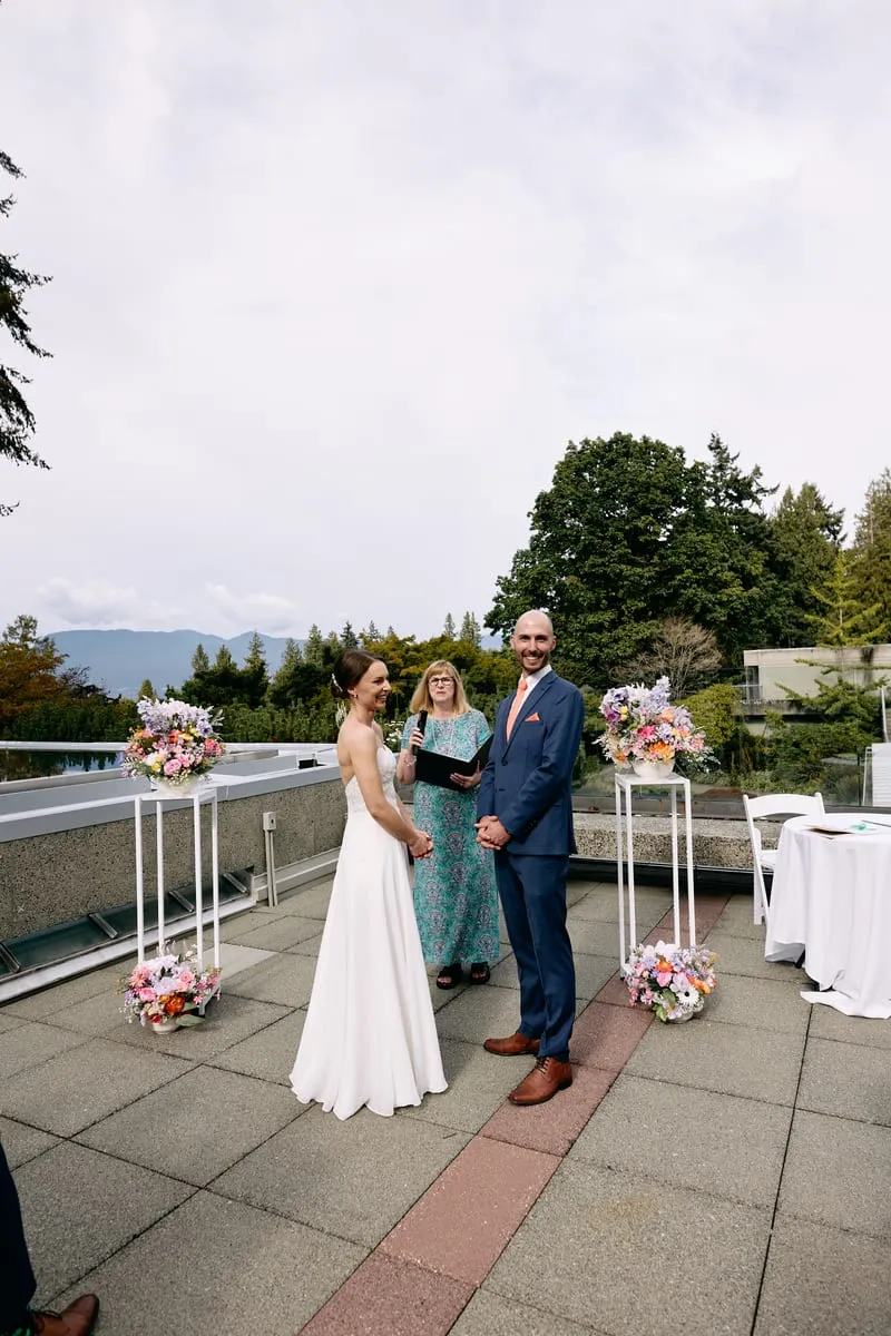 Olivia, James and the officiant stand small under a wide grey sky at the edge of the terrace.