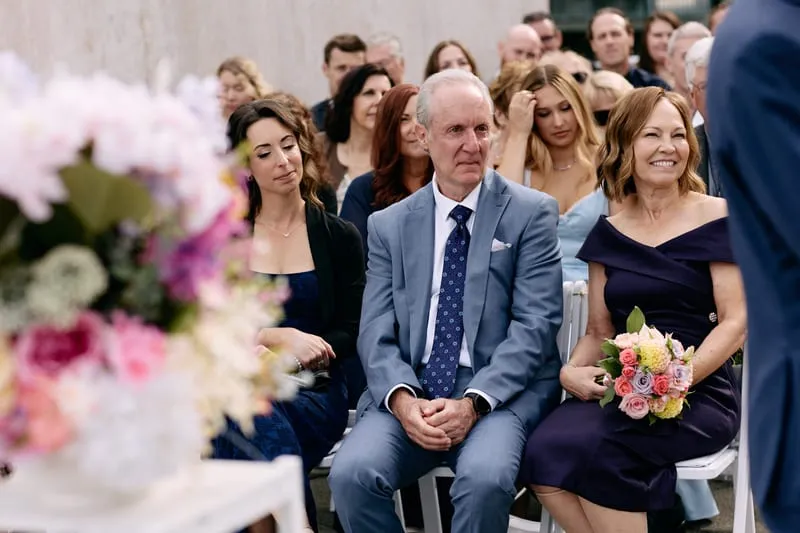Three guests in the front row listen, framed by the flowers along the aisle.